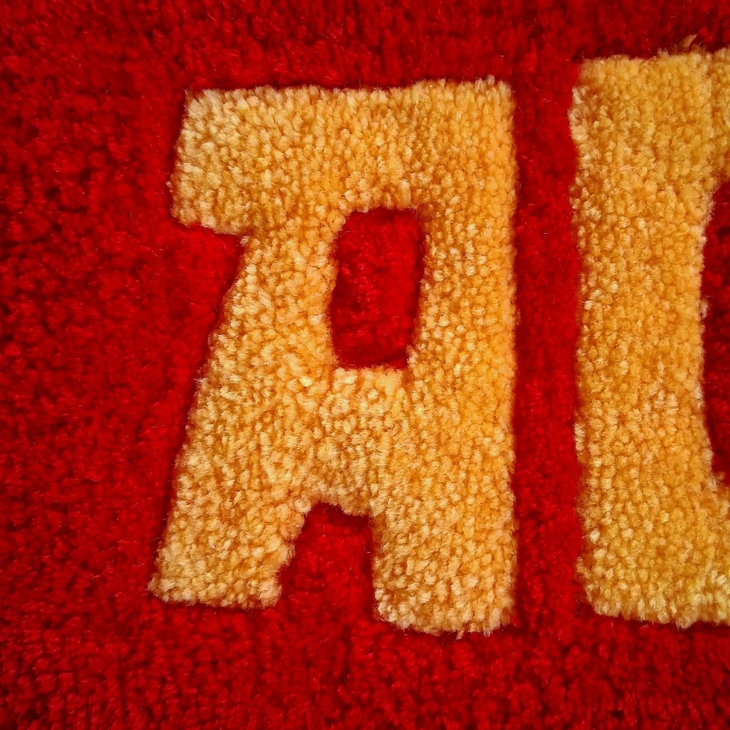 Décoration murale avec l'écriture ADIU écrite en rouge et jaune. Créée par La Balmo Tufting. Laine acrylique