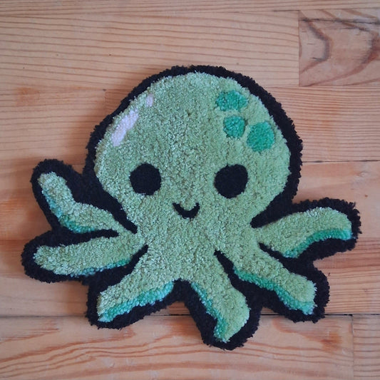 Décoration murale représentant un poulpe vert, souriante. Créée par La Balmo Tufting. Laine acrylique verte et noire