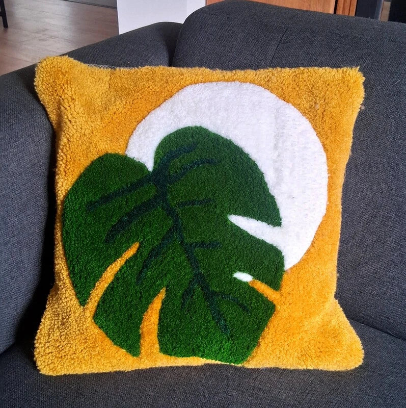 Coussin tufté représentant une feuille de monstera sur une lune blanche et un fond jaune. 