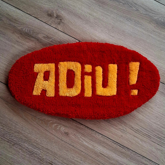 Décoration murale avec l'écriture ADIU écrite en rouge et jaune. Créée par La Balmo Tufting. Laine acrylique