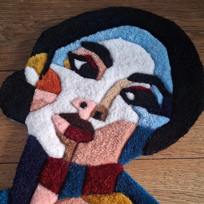 Portrait tufté d'une femme. Une douzaine de couleurs s'agencent pour donner vie à ce visage en laine